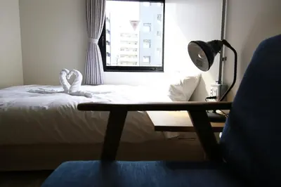 a room with a bed and a table and a window at Wise Owl Hostels Shibuya in Tokyo
