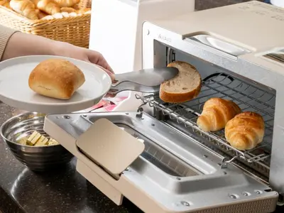 a person holding a plate of bread in a toaster oven at Keio Presso Inn Tokyo Station Yaesu in Tokyo