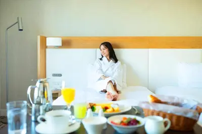 a woman sitting on a bed with a tray of food at Grand Nikko Tokyo Daiba in Tokyo