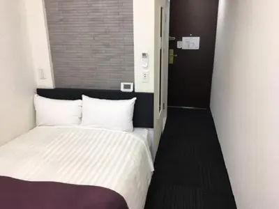 a small bedroom with a bed with white sheets at Ueno Urban Hotel in Tokyo