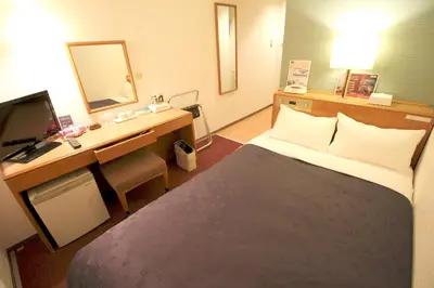 a hotel room with a bed and a desk with a mirror at Smile Hotel Tokyo Shinkoiwa in Tokyo