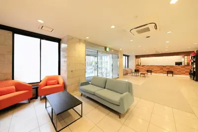 a lobby with a couch and two orange chairs at Smile Hotel Tokyo Ayase Ekimae in Tokyo