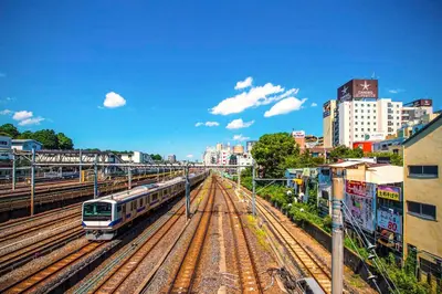 a train on tracks in a city with buildings at Candeo Hotels Ueno Park in Tokyo