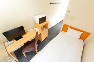 a small room with a desk with a television and a bed at FLEXSTAY INN Sugamo in Tokyo
