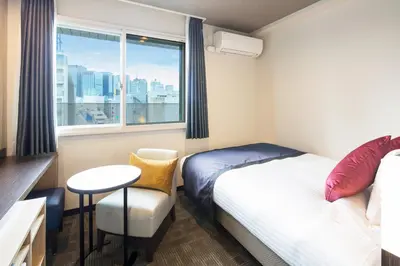 a small room with a bed and a table and a window at HOTEL MYSTAYS Kanda in Tokyo