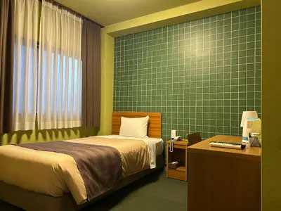 a bedroom with a bed and a desk and a green wall at Tokyo Ueno New Izu Hotel in Tokyo