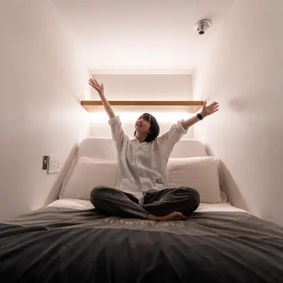 a woman sitting on a bed with her arms in the air at The Millennials Shibuya in Tokyo