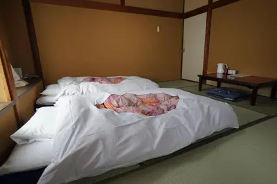 a bedroom with two beds with white sheets and a table at Ryokan Katsutaro in Tokyo
