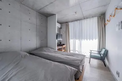 a bedroom with two beds and a chair and a window at bmj Shinjuku Okubo in Tokyo