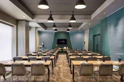 a large room with tables and chairs in front of a screen at MOXY Tokyo Kinshicho in Tokyo