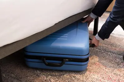 a person pulling a blue suitcase under a bed at Hotel Metropolitan Edmont Tokyo in Tokyo