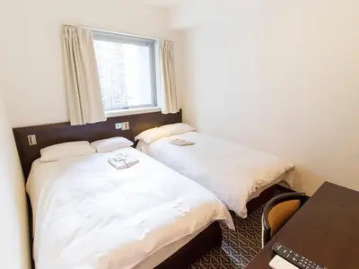 two beds in a room with a desk and a window at Hearton Hotel Higashi-Shinagawa in Tokyo