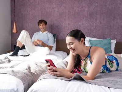 a man and a woman laying on a bed looking at a cell phone at Tokyu Stay Takanawa Shinagawa Area in Tokyo