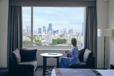 a woman sitting on a chair in a hotel room looking out a window at The Prince Sakura Tower Tokyo, Autograph Collection in Tokyo
