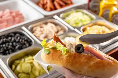 a person holding a sandwich in front of trays of food at HOTEL MYSTAYS Maihama in Urayasu