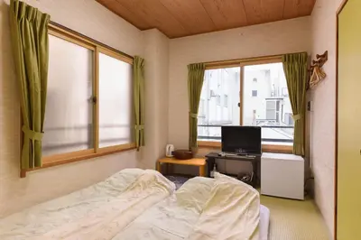 a bedroom with a bed and a tv and windows at Ryokan Mikawaya in Tokyo