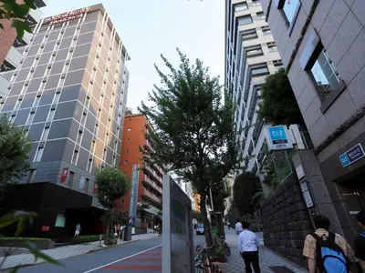a man walking down a city street with tall buildings at Hotel Monterey Hanzomon in Tokyo