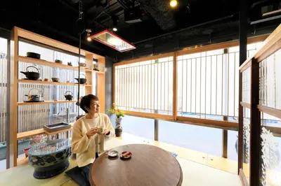 a woman sitting at a table in a room with large windows at Andon Ryokan in Tokyo