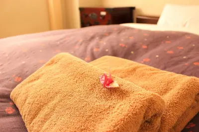 a towel with a flower on it sitting on a bed at K's House Tokyo Oasis - Quality Hostel in Asakusa in Tokyo