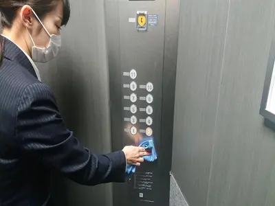 a woman in a mask presses a button on an elevator at Smile Hotel Tokyo Nihonbashi in Tokyo