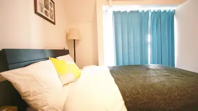 a bedroom with a bed with a blue curtain and a window at Uhome Kanda Hotel in Tokyo