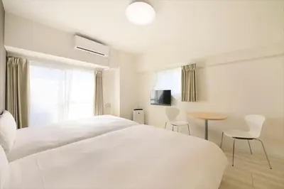 a white bedroom with a bed and a table and chairs at Bay Hotel Urayasu-ekimae in Urayasu