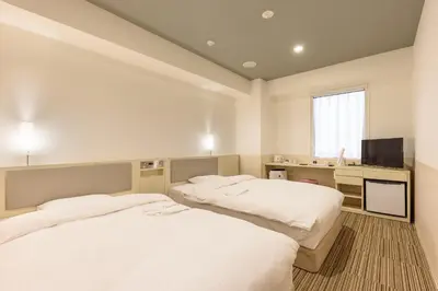 two beds in a room with a desk and a television at Belken Hotel Kanda in Tokyo