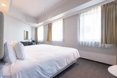 a white bedroom with a large white bed and windows at E Hotel Higashi Shinjuku in Tokyo