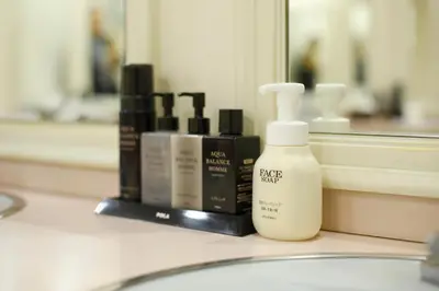 a bathroom counter with a bottle of lotion and other cosmetics at Shinjuku Kuyakusho-mae Capsule Hotel in Tokyo