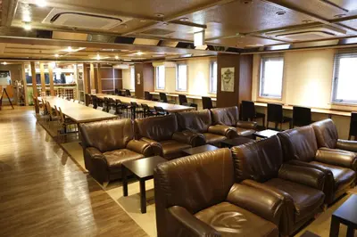 a room with leather couches and tables and chairs at Shinjuku Kuyakusho-mae Capsule Hotel in Tokyo