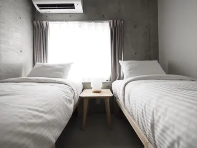 two twin beds in a room with a window at Smi:re Stay Oshiage in Tokyo