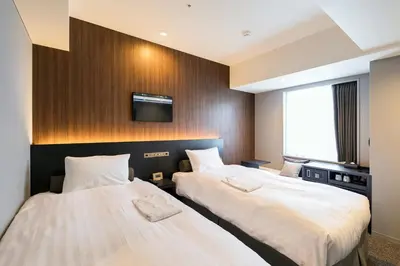 two beds in a hotel room with a tv on the wall at Ginza Capital Hotel Moegi in Tokyo