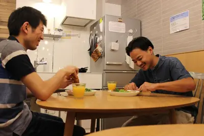 two men sitting at a table eating food at plat hostel keikyu asakusa station in Tokyo