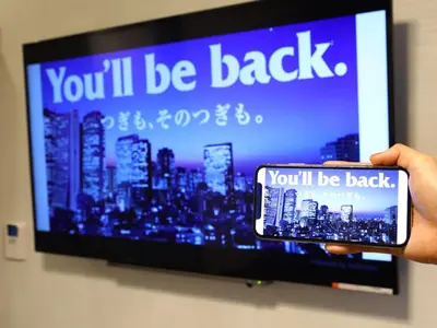 a person holding a cell phone in front of a tv at APA Hotel Kodemmacho Ekimae in Tokyo