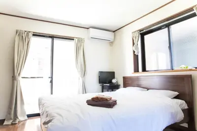 a bedroom with a bed with white sheets and windows at Tokyo Aoto House in Tokyo