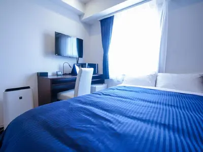 a bedroom with a blue bed with a desk and a window at HOTEL LiVEMAX Tokyo Shiomi Ekimae in Tokyo