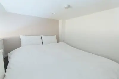 a white bed in a small white room at GLOU Higashi Shinjuku in Tokyo
