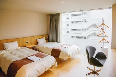 a hotel room with two beds and a chair and a window at Hotel Comfact in Tokyo