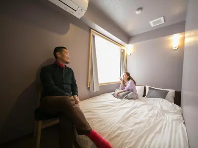 a man and a girl sitting on a bed looking out a window at THE WARDROBE Hotel Shimokitazawa in Tokyo