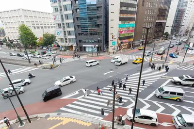a busy city street with cars and people crossing a crosswalk at Matsui Building in Tokyo