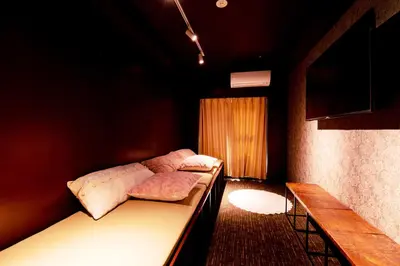 a dark room with two beds and a bench at bnb+ Ueno Okachimachi in Tokyo
