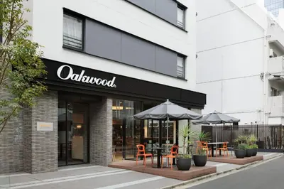 a restaurant with tables and umbrellas in front of a building at Oakwood Apartments Nishi-Shinjuku Tokyo in Tokyo