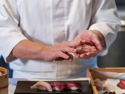 a chef holding a piece of food in his hands at Mitsui Garden Hotel Ginza-gochome in Tokyo