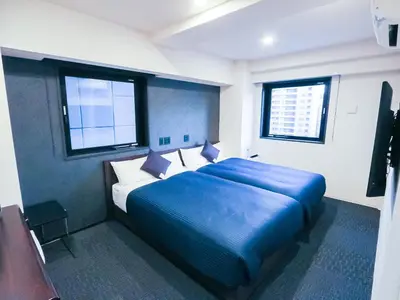a bedroom with a large blue bed with two windows at HOTEL LiVEMAX Tokyo Shintomicho in Tokyo
