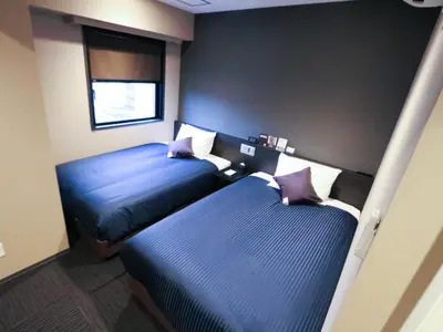 two beds in a room with blue sheets and purple pillows at HOTEL LiVEMAX Tokyo-Otsuka Ekimae in Tokyo