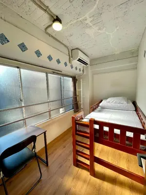 a bedroom with a bed and a chair and windows at Nomad Hostel East in Tokyo