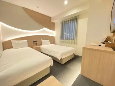 a bedroom with two beds and a desk with a laptop at Henn na Hotel Premier Tokyo Asakusa Tawaramachi in Tokyo
