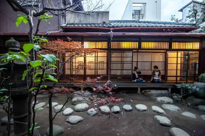 two people sitting on a bench in front of a building at Guesthouse toco in Tokyo