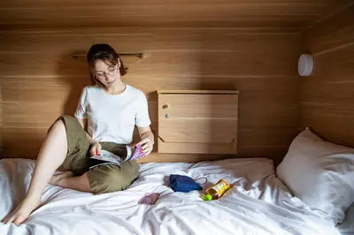 a woman sitting on a bed reading a book at Grids Tokyo Ueno Hotel&Hostel in Tokyo