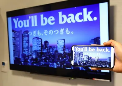 a person holding a cell phone in front of a tv at APA Hotel Ayase Ekimae in Tokyo